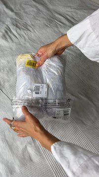 Imballaggio in plastica trasparente che contiene un indumento, con un codice a barre giallo e molteplici etichette che mostrano informazioni sul prodotto e avvertenze di sicurezza.