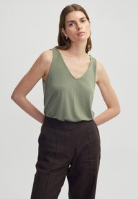 Olijfgroene mouwloze top met een V-hals ontwerp, gemaakt van zachte stof, gecombineerd met donkerbruine hoge taillebroeken. Glad textuur en comfortabele pasvorm.