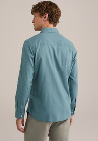 Türkiz színű, hosszú ujjú ing gallérral, hátpanel részletekkel és gombos mandzsettákkal, puha anyagból készült, lekerekített aljjal.