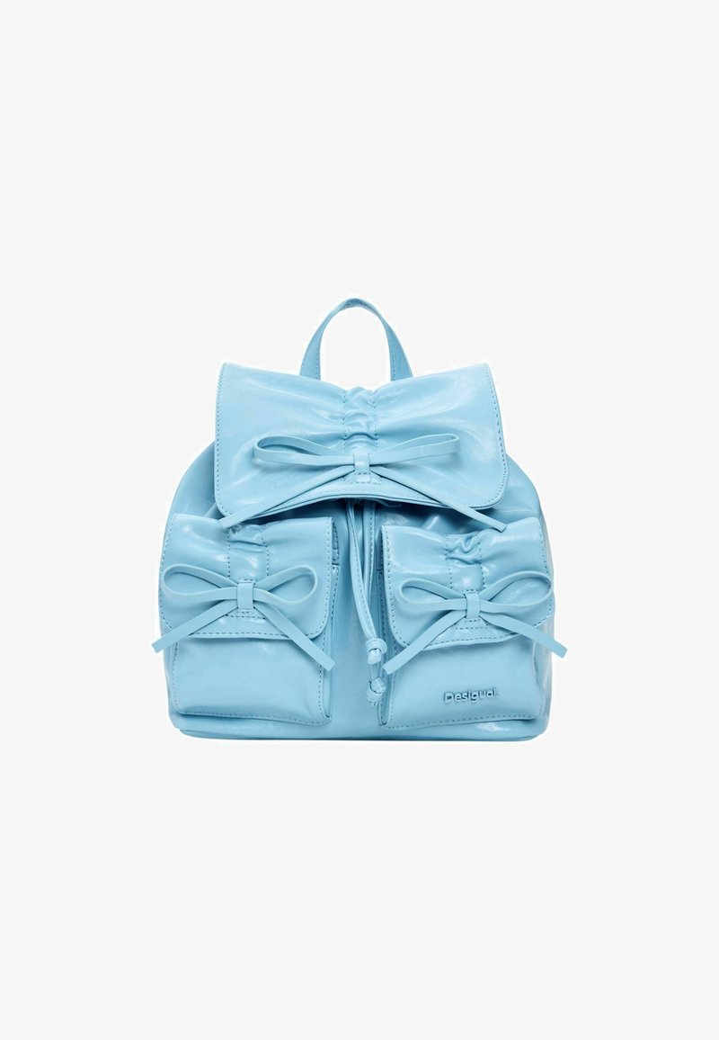 Sac à main bleu clair conçu comme un petit sac à dos, avec un grand nœud, deux poches avant ornées de nœuds, et une finition brillante et texturée.