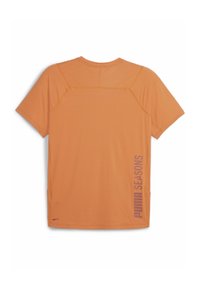 Orange sports t-shirt med korte ærmer, flade sømme og sideskår. Har "PUMA SEASONS" trykt i lilla på højre side.