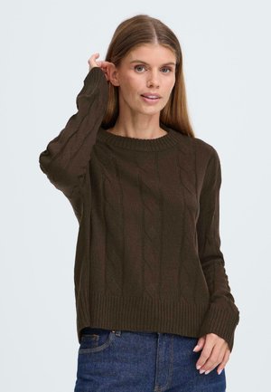 Brun strikket genser med kabelstrikkedesign, ribbet rund hals, og lange ermer, kombinert med mørkeblå jeans.