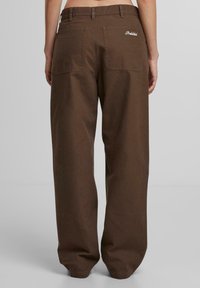 Braune Baumwolle weite Hose mit zwei Gesäßtaschen und gesticktem Markenlabel. Schlichtes Design mit glatter Textur.