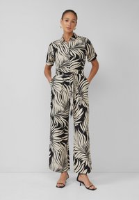 Zwart en beige jumpsuit met een bladerenpatroon, korte mouwen, een knoopsluiting aan de voorkant en een cinched riem in de taille. Ontwerp met wijde benen.