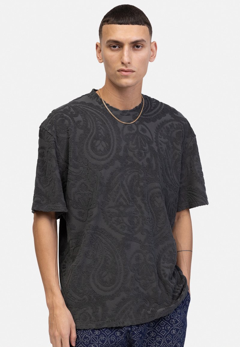 Mørk grå kortærmet t-shirt med struktureret paisley-mønster, rund halsudskæring og løs pasform. Bæres med mønstrede blå bukser.