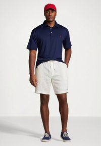 Tamsiai mėlynas polo marškinėlis, balti lininiai šortai, raudona beisbolo kepuraitė ir mėlynos sportbačiai. Trumpomis rankovėmis, laisvas stilius. Paprastas dizainas be raštų ar akcentų.