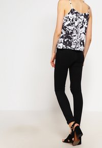 Czarnobiały top bez rękawów w wzory z cienkimi ramiączkami, zestawiony z czarnymi obcisłymi jeansami i czarnymi szpilkami z ozdobną klamrą.