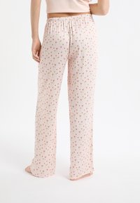Jasnoróżowe spodnie do piżamy o miękkiej teksturze, z elastycznym pasem i wzorem małych czerwonych serc oraz złotych kwiatów. Luźny krój.