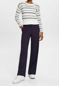 Pull en maille blanche à rayures bleu marine, associé à un pantalon large violet foncé et des baskets blanches. Texture légère avec des détails en maille ajourée.