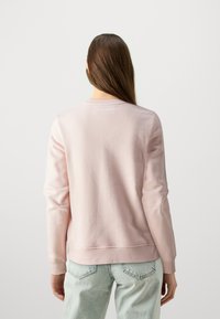 Sweatshirt rosa con vestibilità rilassata, polsini e orlo a coste, con il logo "KARL LAGERFELD" in bianco sulla parte posteriore del collo. Leggera texture in fleece.
