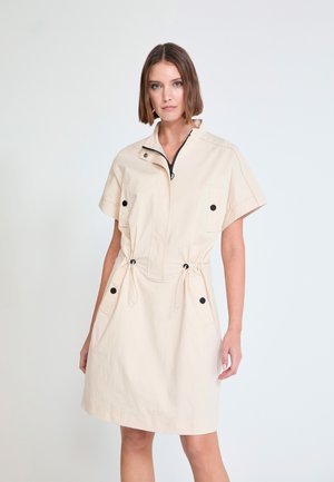 Vestido beige de manga corta hecho de tela ligera, con cuello con cremallera, cintura con cordón y detalles de botones negros.