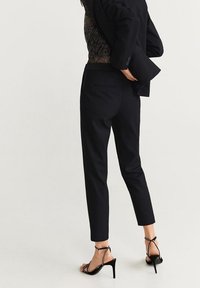 Czarne dopasowane spodnie o tapered kształcie, wykonane z gładkiego materiału, w połączeniu z czarnymi sandałami na wysokim obcasie z zapięciem na kostce.