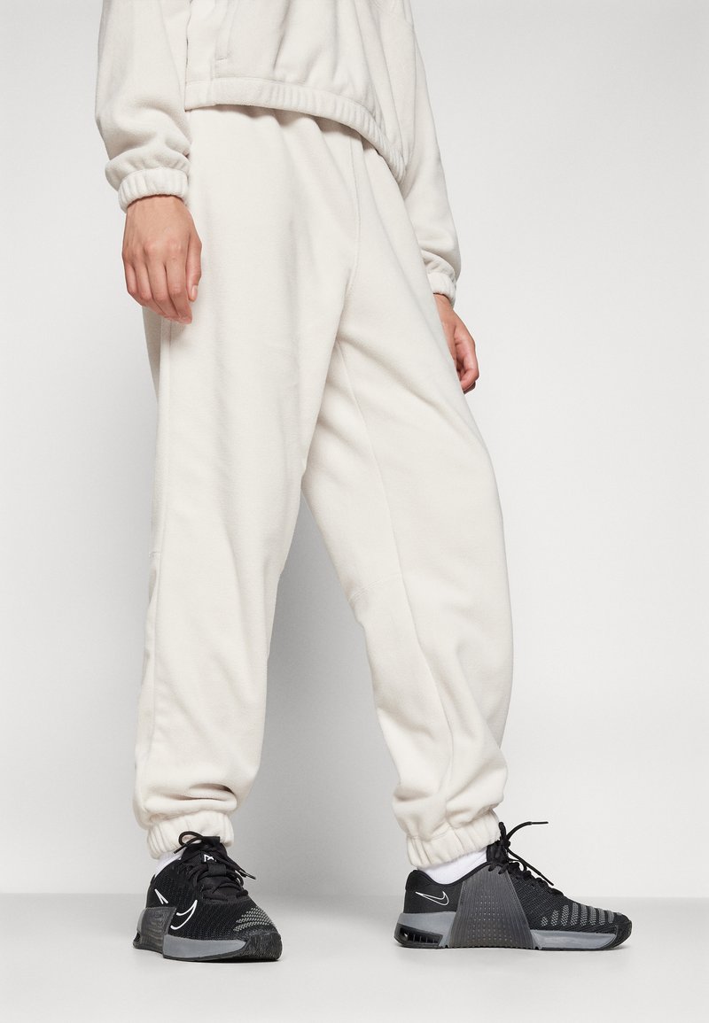 Jasno beżowe, miękkie dresy z elastycznymi mankietami i paskiem w talii, w połączeniu z czarnymi butami sportowymi z teksturowaną cholewką i szarymi akcentami.