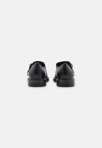 Chaussures en cuir noir à finition lisse, bout arrondi et petit talon. Elles présentent un design simple avec des détails de couture minimalistes.