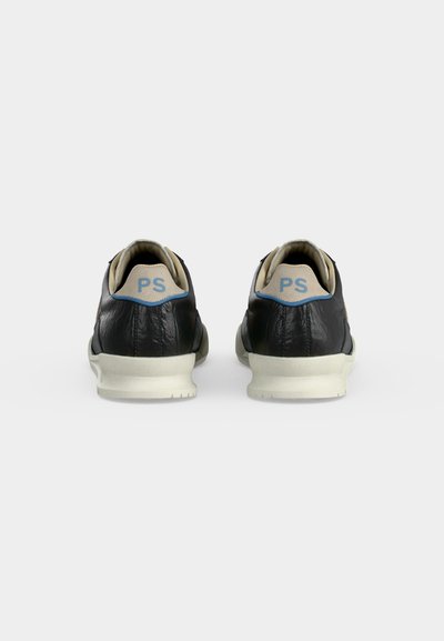 Ζευγάρι μαύρα δερμάτινα sneakers, εμφανιζόμενα από πίσω με μπεζ λωρίδες στη φτέρνα που φέρουν μπλε γράμματα "PS" και λευκές σόλες.
