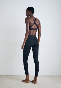 Soutien-gorge de sport noir avec un design à dos croisé, associé à des leggings noirs taille haute. Texture lisse avec un ajustement serré, sans motifs visibles.