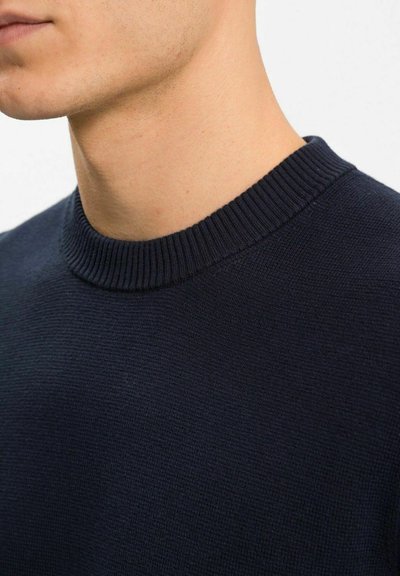 Mörkblå stickad tröja med ribbad rund hals. Slät textur, figurnära design och subtilt mönster i hela tyget.