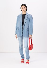 Svetlo modra oversize denim jakna z dvema sprednjima žepoma, v completa z oprijetimi svetlo modrimi kavbojkami, rdečo torbico in rdečimi čevlji s koničastim prstom.