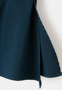 Tissu bleu foncé avec un détail d'ouverture verticale, montrant la texture et les coutures le long des bords sur un fond clair.