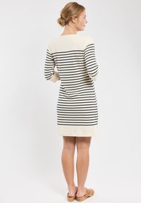 Abito a righe in crema e blu navy, con maniche lunghe, scollatura a barca e silhouette dritta che arriva sopra il ginocchio.