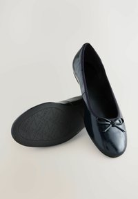 Ballerines navy avec une finition brillante, ornées d'un petit nœud, aux bords doux et avec une semelle noire texturée portant un logo.