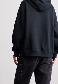 Sudadera negra con capucha y un ajuste holgado, con hombros caídos y puños acanalados, combinada con pantalones cargo gris oscuro con bolsillos.