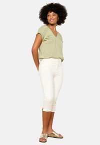 Top verde claro en forma de V con un brillo sutil, combinado con jeans blancos cortos y sandalias doradas de tiras cruzadas. Diseño simple, textura suave.