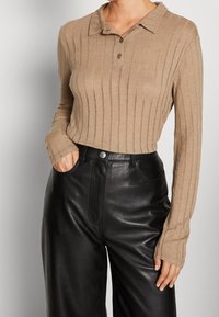 Beige ribbed pitkähihainen polo paita, jossa on kaulus ja kolme nappia, yhdistettynä mustiin tekonahkaisiin leveälahkeisiin housuihin, joissa on etul pockets.
