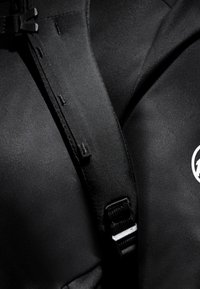 Svart textilharnes med justerbara remmar, en plastspänne och texturerade ytor. Framträdande logotyp på ena sidan.