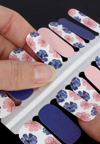 Des enrouleurs d'ongles avec des motifs floraux en rose, violet et blanc, accompagnés de couleurs unies bleu marine et rose ; présentés sur une carte avec un doigt tenant un enrouleur.