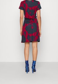 Robe à motif floral rouge et marine avec des manches courtes et une taille ajustée, associée à des bottines bleues brillantes, mettant en avant un design épuré.