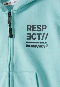 Svetlozelená mikina na zips s čiernym grafickým potlačou, ktorá obsahuje slovo "RESPECT" a detaily "SINCE 96" a "96.RSP/ACV 3." Mäkka textúra.