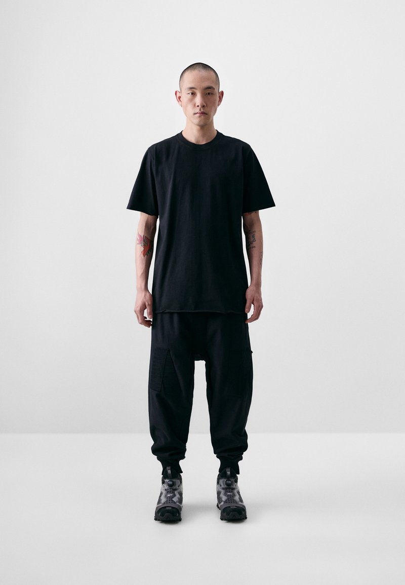 Black cotton T-shirt with a relaxed fit, paired with loose black cargo pants featuring multiple pockets. Footwear: gray patterned shoes.