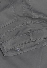 Gray cotton fabric with a smooth texture features multiple stitched pockets and a clear button at the waistband.