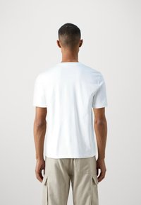 T-shirt bianco in cotone con collo rotondo e maniche corte, mostrato da dietro. Tessuto texturizzato, design aderente, senza motivi o grafiche visibili.