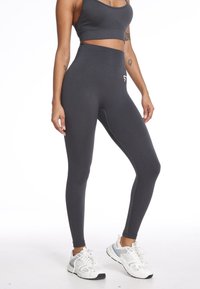 Szare legginsy z wysokim stanem, wykonane z elastycznej tkaniny, charakteryzujące się gładką teksturą i dyskretnym logo. W zestawie z białymi butami sportowymi.