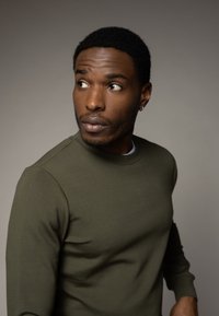 Felpa verde oliva con scollo rotondo, maniche aderenti e polsini a coste, realizzata in un morbido tessuto testurizzato. Modello che guarda leggermente a sinistra.