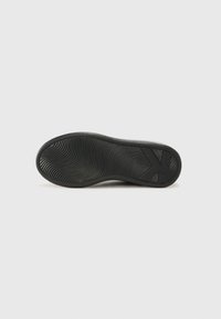 Semelle de chaussure en caoutchouc noir avec un motif de semelles ondulées et un logo en relief. Forme plate conçue pour l'adhérence et la durabilité.
