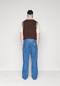 Brown knitted vest over a light beige short-sleeve shirt, paired with loose blue jeans. Simple design with ribbed texture and a casual fit.