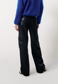 Pantalons cargo en cuir noir avec jambes larges, deux poches latérales et coutures ton sur ton, associés à un pull texturé bleu.