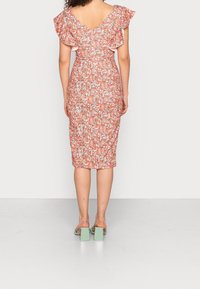 Robe ajustée à imprimé floral orange avec des manches à volants et un dos en V. Portée avec des sandales à talons carrés vert menthe.