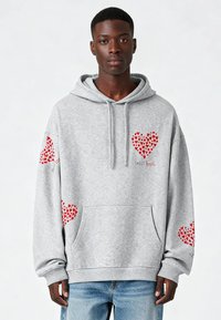 Siv hoodie z več rdečimi srčnimi vzorci, sprednjim žepom in kapuco s vrvico. Narejen iz mehkega materiala z rebrastimi manšeti in robom.