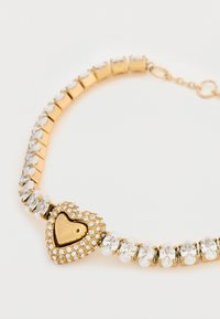 Βραχιόλι σε χρυσό χρώμα με κρεμαστό καρδιά διακοσμημένη με καθαρούς στρας. Λείες συνδέσεις με οβάλ πέτρες δημιουργούν ένα λαμπερό εφέ.