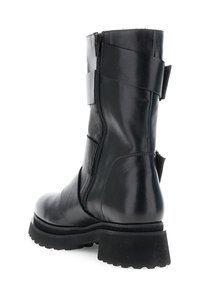 Bota de cuero negro que llega a la mitad de la pantorrilla, con cremallera lateral, suela gruesa y texturizada, y una correa decorativa ancha alrededor de la parte superior.