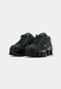 Par crnih Nike tenisica za trčanje s opružnim potpeticama i vezanjem na bijeloj pozadini.