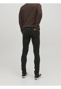 Vaqueros ajustados negros con una textura desgastada, cintura alta y bolsillos traseros, combinados con zapatillas negras y blancas y un suéter marrón.