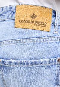 Poche en denim bleu clair avec un patch en cuir beige portant la mention "DSQUARED2 Twins' Jeans" et de légers détails effilochés.