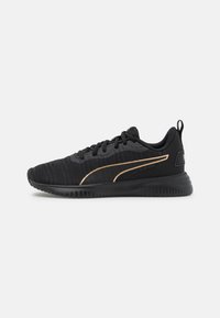 Zapatillas deportivas negras con parte superior de textil tejido, acentos dorados en los laterales, collar acolchado y suela de goma texturizada. Diseño minimalista.