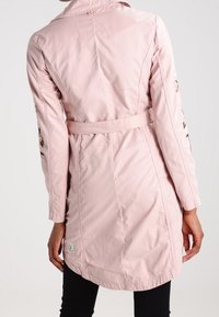 Růžový lehký kabát s páskem v pase, dlouhými rukávy a dekorativními detaily na rukávech, navržený pro volný střih.