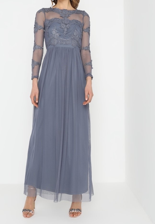 Lång, grå klänning med en genomskinlig bodice, detaljer i spets och långa ärmar. En flödande kjol kompletterar de dekorerade accenterna vid halsringningen.